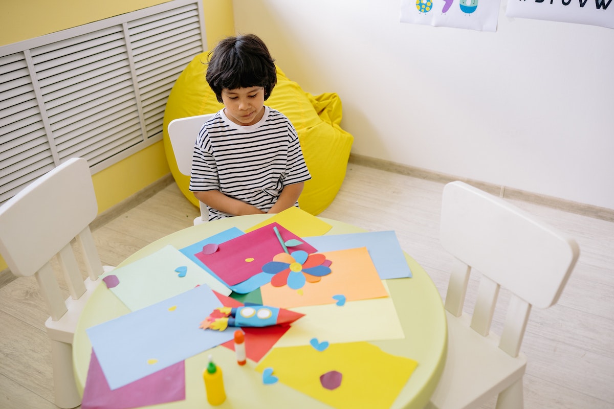 Copil cu hartie colorata pe masa